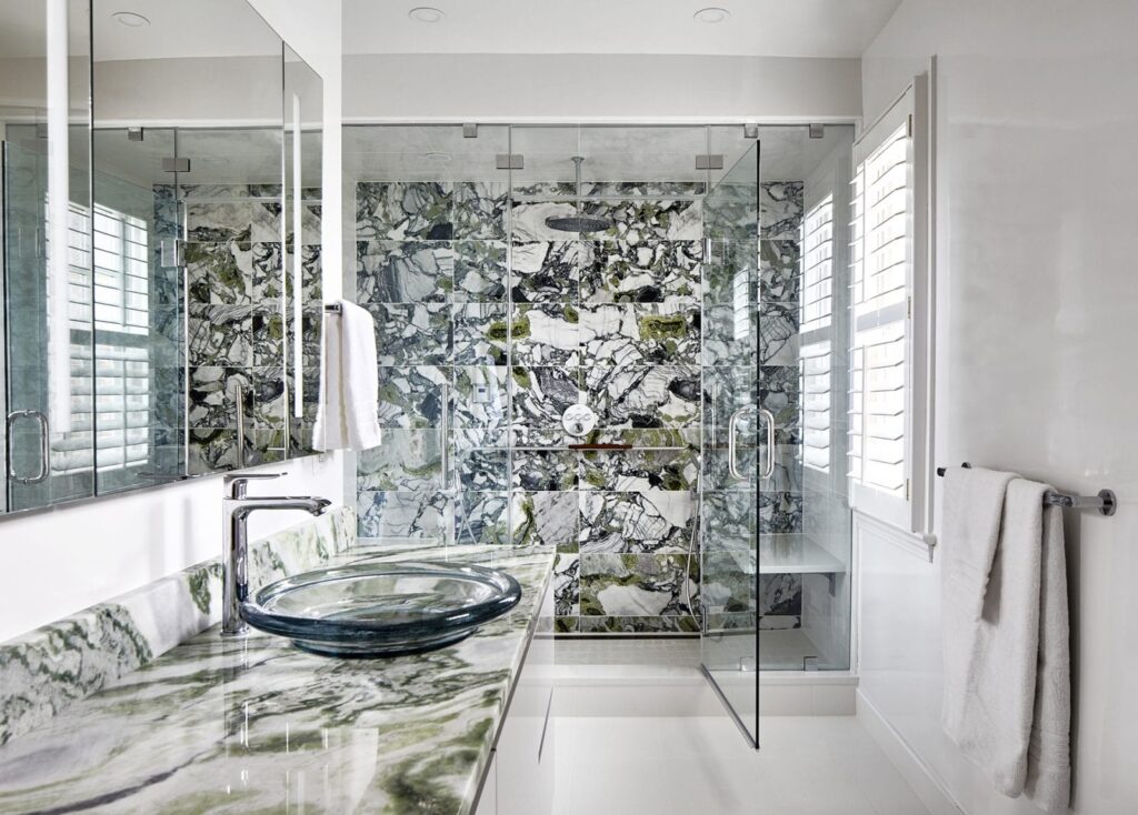 Luxury bathroom featuring a custom glass swinging enclosure with marble walls and modern fixtures.