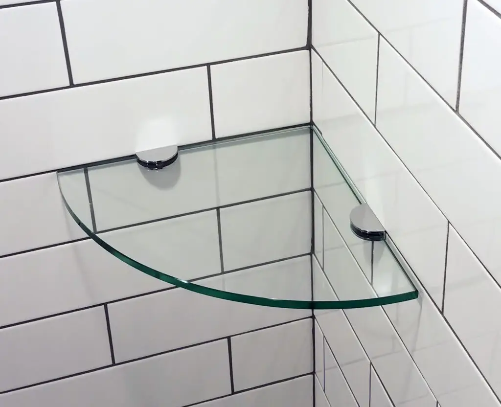 Glass corner shelf mounted on white tiled wall with chrome brackets.