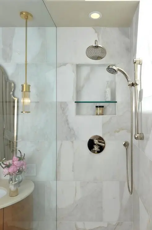 Luxurious shower area with marble tiles, gold fixtures, and a built-in glass shelf.