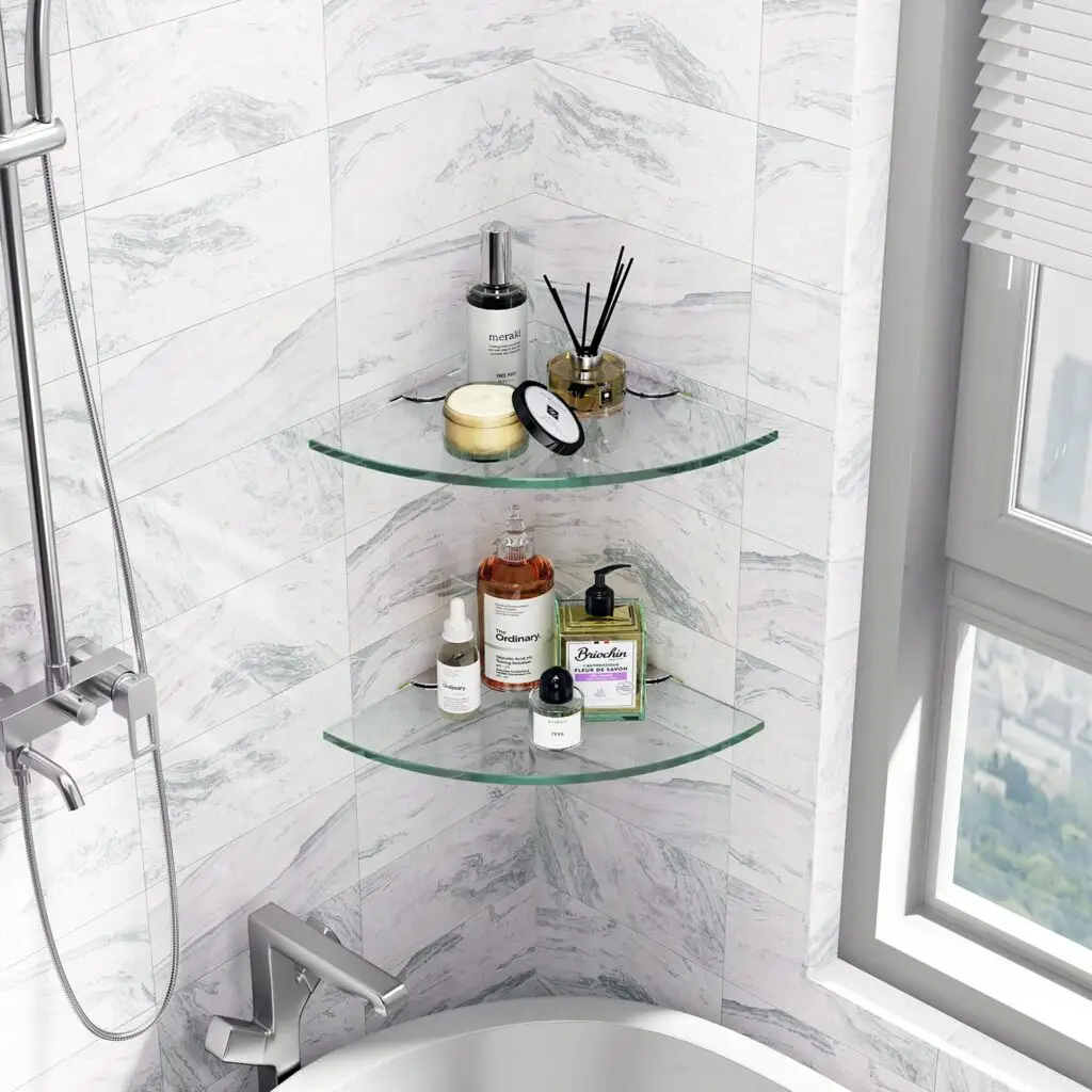 Corner glass shelves in a bathroom holding toiletries and decor items.