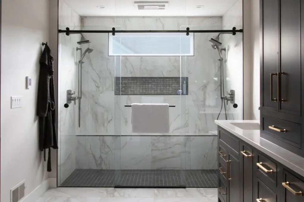 Sleek and modern frameless sliding glass shower enclosure with a black barn-style track, featuring a spacious dual showerhead design and elegant marble walls.